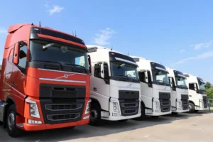 Row of parked Volvo semi trucks, with a red truck in front and white trucks behind it