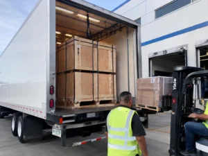 Forklift unloading strapped wooden crates from a delivery truck at a warehouse dock