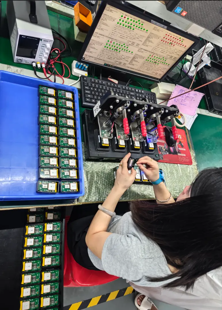 Technician assembling and testing circuit boards at a workbench with a computer monitor and test fixture
