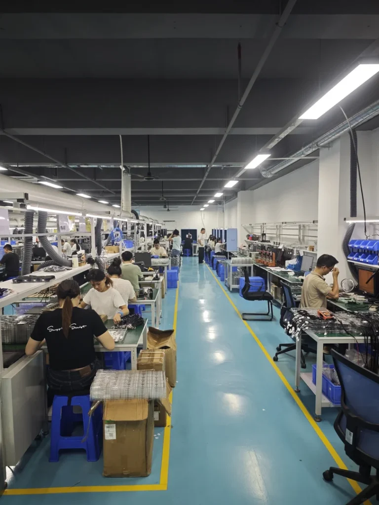 Workers assembling electronics at benches in a factory workspace