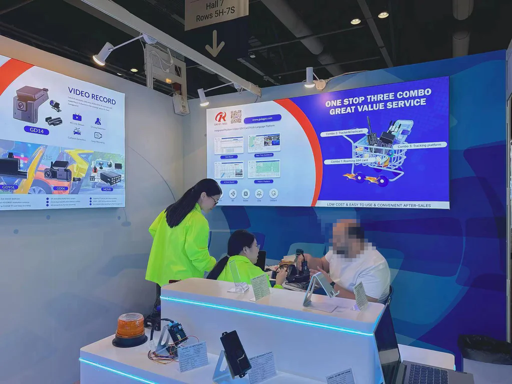 Trade show booth displaying video recorders and a “One Stop Three Combo” tracking service, with staff assisting visitors